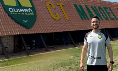 Lucas Barezani posa sorrindo em frente ao prédio do CT Manoel Dresch, centro de treinamento do Cuiabá Esporte Clube, vestindo camisa oficial de treino do clube.