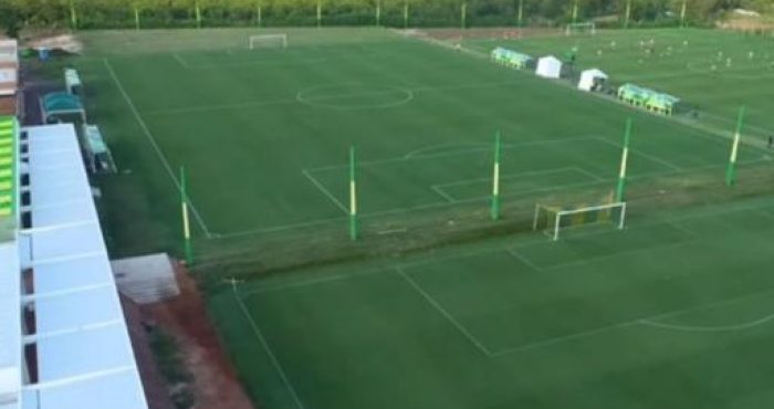 Foto do exterior do novo CT do Cuiabá EC: "Vista do novo Centro de Treinamento do Cuiabá EC, com instalações modernas e campo de treino ao fundo, representando o futuro do time.