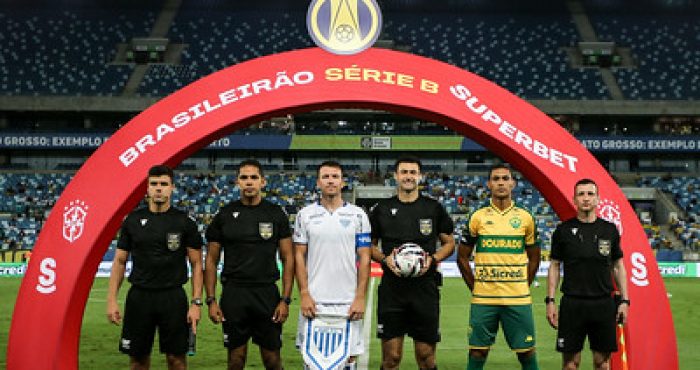 Capitães de Cuiabá e Avaí, ao lado da equipe de arbitragem, posam para a foto oficial sob o arco do Brasileirão Série B Superbet, momentos antes do início da partida na Arena Pantanal.
