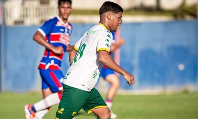Jogador do Cuiabá Sub-20 conduz a bola durante partida contra o Fortaleza, usando uniforme branco e verde, com adversário ao fundo vestindo o uniforme tricolor do time cearense, em jogo válido pelo Campeonato Brasileiro Sub-20.