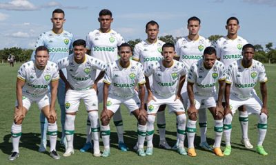 Jogadores do Cuiabá posando para a foto oficial do time, alinhados no campo com seus uniformes completos. Eles exibem sorrisos e demonstram união, enquanto estão em posição para a foto em grupo, representando a equipe de futebol do Cuiabá Esporte Clube