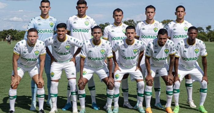 Jogadores do Cuiabá posando para a foto oficial do time, alinhados no campo com seus uniformes completos. Eles exibem sorrisos e demonstram união, enquanto estão em posição para a foto em grupo, representando a equipe de futebol do Cuiabá Esporte Clube
