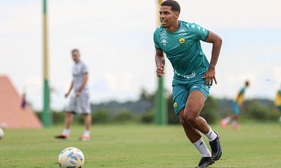 Atacante Eliel do Cuiabá corre com a bola durante treino em campo, vestindo uniforme verde e focado na jogada.