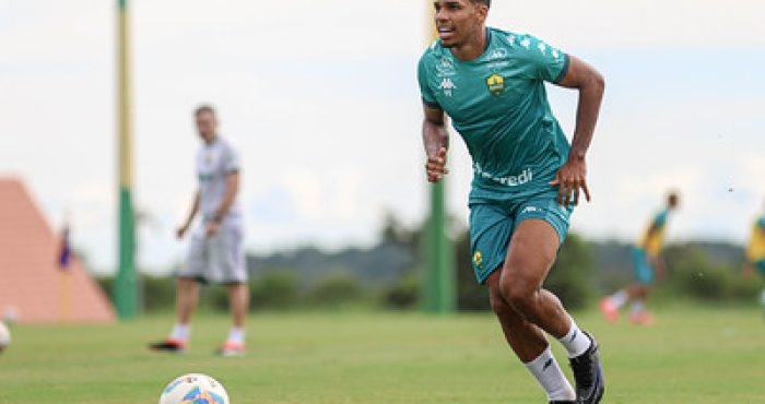 Atacante Eliel do Cuiabá corre com a bola durante treino em campo, vestindo uniforme verde e focado na jogada.