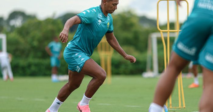 "Emerson Negueba durante treino com uniforme de treino verde do Cuiabá, realizando exercício de agilidade no gramado."