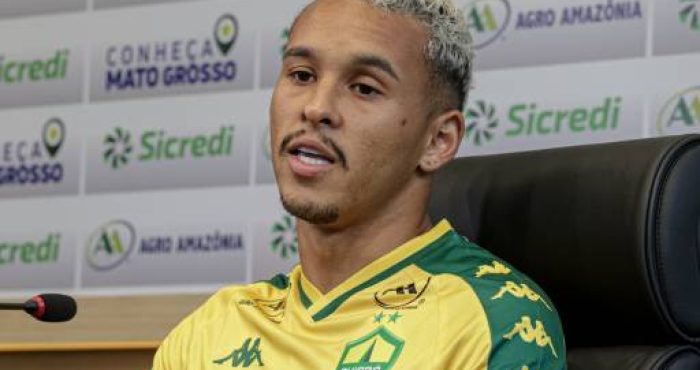 Entrevista com Juan Christyan, jogador do Cuiabá EC, falando sobre a preparação do time. Ele veste o uniforme oficial do clube e responde às perguntas dos jornalistas em uma coletiva de imprensa.