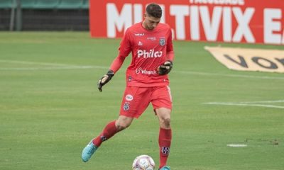 "Goleiro Guilherme Nogueira, do Capivariano, durante partida, vestindo uniforme vermelho e dominando a bola com os pés em campo de futebol."