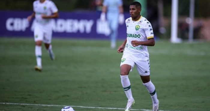 Jogador do Cuiabá Sub-20 conduz a bola durante partida do Campeonato Brasileiro Sub-20, vestindo uniforme branco com detalhes verdes e a braçadeira de capitão.
