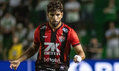 Pepê, volante de futebol, em ação com a camisa do Vitória durante partida, correndo em campo e observando o jogo.