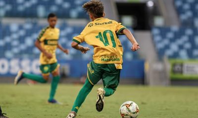Jogadores do Cuiabá Sub-13 se preparando para a disputa da Liga de Desenvolvimento, com a tabela da competição à vista, simbolizando a entrada do time na elite do futebol infantil.